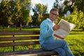 Serious bearded mature man reading daily newspaper on park bench