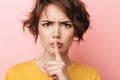 Serious beautiful woman posing over pink wall background showing silence gesture