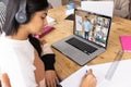 Serious biracial teenage girl writing in book while learning online over video call on laptop Royalty Free Stock Photo