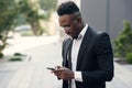 Serious black businessman texting on smartphone outdoors. Young african-american salesman working with mobile near Royalty Free Stock Photo