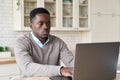 Serious black businessman working remotely from homeoffice on laptop computer.