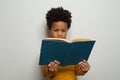 Serious black kid boy reading a book on white background