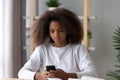 Serious black teen girl using smartphone while studying