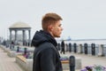 A serious blond man in a leather jacket stands on the city embankment against the backdrop of a rotunda. Side view. Blur the