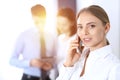 Serious blonde businesswoman talking by phone in the background of her colleagues in office. Business concept