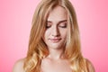 Serious blonde female with appealing apearance looks down, has shy expression, isolated over pink background. Good looking young w Royalty Free Stock Photo