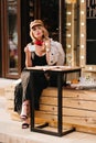 Serious blonde girl in black shoes chilling in outdoor cafe and enjoying tea. Attractive young woman wears stylish Royalty Free Stock Photo