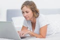 Serious blonde woman lying on bed using laptop Royalty Free Stock Photo