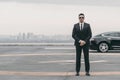 serious bodyguard standing with sunglasses and security earpiece on helipad and looking