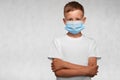 Serious boy with crossed arms weared in surgical mask and white t-shirt on a white background. Covid-19, flu, or pollution