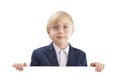 Serious boy with empty white paper board and laughs. Cute blond boy peeking out from behind white board. Space for text Royalty Free Stock Photo
