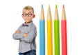 Serious boy in glasses and bowtie posing near huge colorful pencils. Educational concept. Isolated over white.