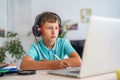 Serious boy with headphones uses a laptop to study online, do homework