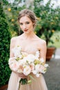 Serious bride in a pink dress with a bouquet of flowers on a background of a green tree in a tub. Lake Como