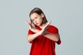 Serious brunette teen girl shows cross stop gesture, looking unamused, saying no, forbid something, standing over grey background