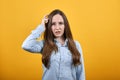 Serious brunette woman in denim blue shirt keeping hand on head, thinking Royalty Free Stock Photo