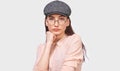 Serious brunette young woman wears transparent spectacles, casual pink shirt and gray cap, looks seriously directly into camera Royalty Free Stock Photo