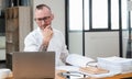 Serious business man using laptop sitting at the table in a home office, looking at the paper, communicating online Royalty Free Stock Photo