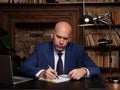 Serious business man working on documents, makes an entry in the diary with notebook and lamp on the table. Home office library in Royalty Free Stock Photo