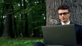 Serious business man working on laptop, sitting under tree in central park Royalty Free Stock Photo