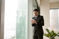 Serious businessman holding tablet standing near big window in o Royalty Free Stock Photo