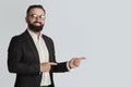 Serious businessman in office wear tand glasses smiling and pointing aside on light grey background, space for you ad