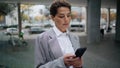 Serious businesswoman messaging smartphone on street. Focused woman typing cell