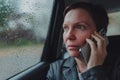 Serious businesswoman talking on mobile phone from the backseat of the car during the rain Royalty Free Stock Photo