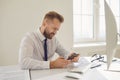 Serious busy businessman reads message on the phone at a table with a computer in the office. Royalty Free Stock Photo