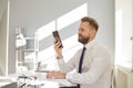 Serious busy businessman reads message on the phone at a table with a computer in the office. Royalty Free Stock Photo