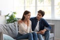 Serious careful young european guy calms upset unhappy lady in living room interior