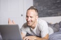 Serious casual young man using laptop in bed at home Royalty Free Stock Photo