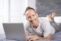 Serious casual young man using laptop in bed at home Royalty Free Stock Photo
