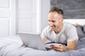 Serious casual young man using laptop in bed at home Royalty Free Stock Photo