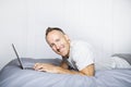 Serious casual young man using laptop in bed at home Royalty Free Stock Photo