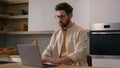 Serious Caucasian man browsing internet service chatting online in social media renter with laptop at kitchen food Royalty Free Stock Photo