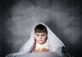 Serious child with flashlight hiding under blanket