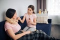 Serious child sit on couch with sick mother. She give her some syrup. Young woman take it with mouth. They sit together