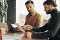 Serious company workers looking through document, collaborating, using laptop at modern office, copy space