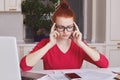 Serious concentated female worker surrounded with documents, tries to gather with thoughts and make business report, sits over kit