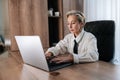 Serious concentrated attractive middle-aged business woman sitting in modern light office at desk working on laptop Royalty Free Stock Photo