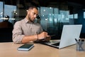 Serious concentrated businessman writing document while sitting in office using laptop for online learning, hispanic man Royalty Free Stock Photo