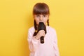 Serious and concentrated little girl singing or talking in microphone isolated on yellow background, child with pigtails Royalty Free Stock Photo