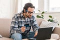 Serious concentrated young caucasian male shopaholic in glasses sits on sofa with computer and credit card