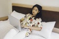 Serious concentrated young woman working from the bed. Hold the laptop on the knees and type on the keyboard