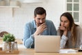 Serious concerned couple sit indoor looking at laptop read news