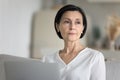 Serious concerned middle-aged woman sit on sofa with laptop