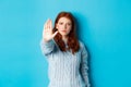 Serious and confident redhead girl telling to stop, saying no, showing extended palm to prohibit action, standing over