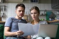 Serious confused couple checking domestic bills with papers and