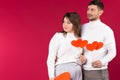 Serious couple with lbig cardboard red hearts are looking away. Red background, empty side space for you advertisement